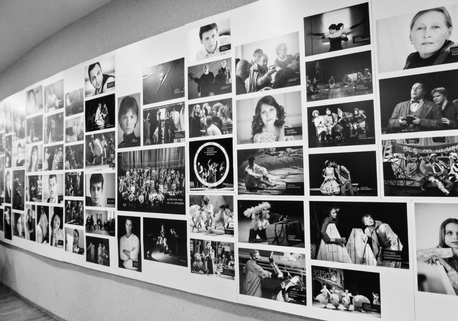 A long corridor wall covered in black-and-white photographs of faces, groups and stage scenes, receding into the distance